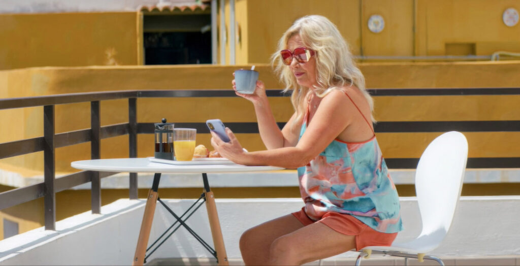 En sommarklädd kvinna sitter på en terrass och äter frukost.