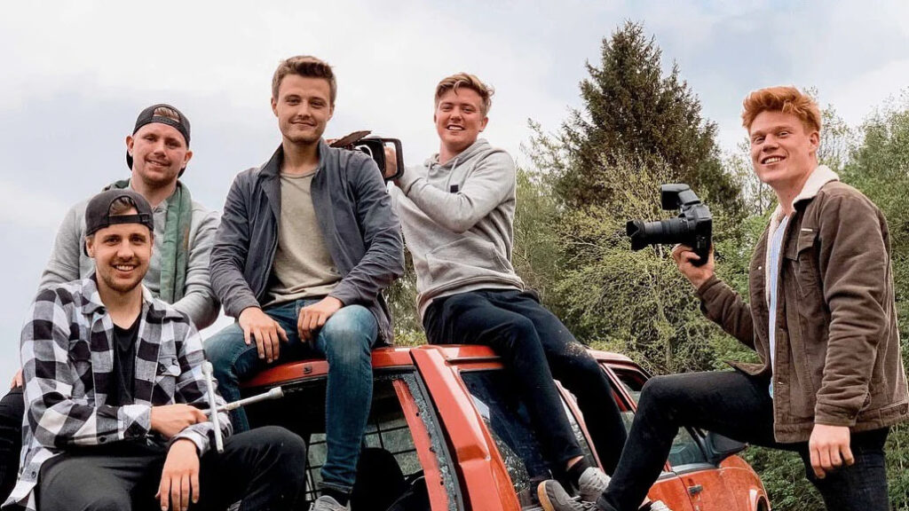 Fem killar sitter på en röd Volvo, en håller en kamera i handen.